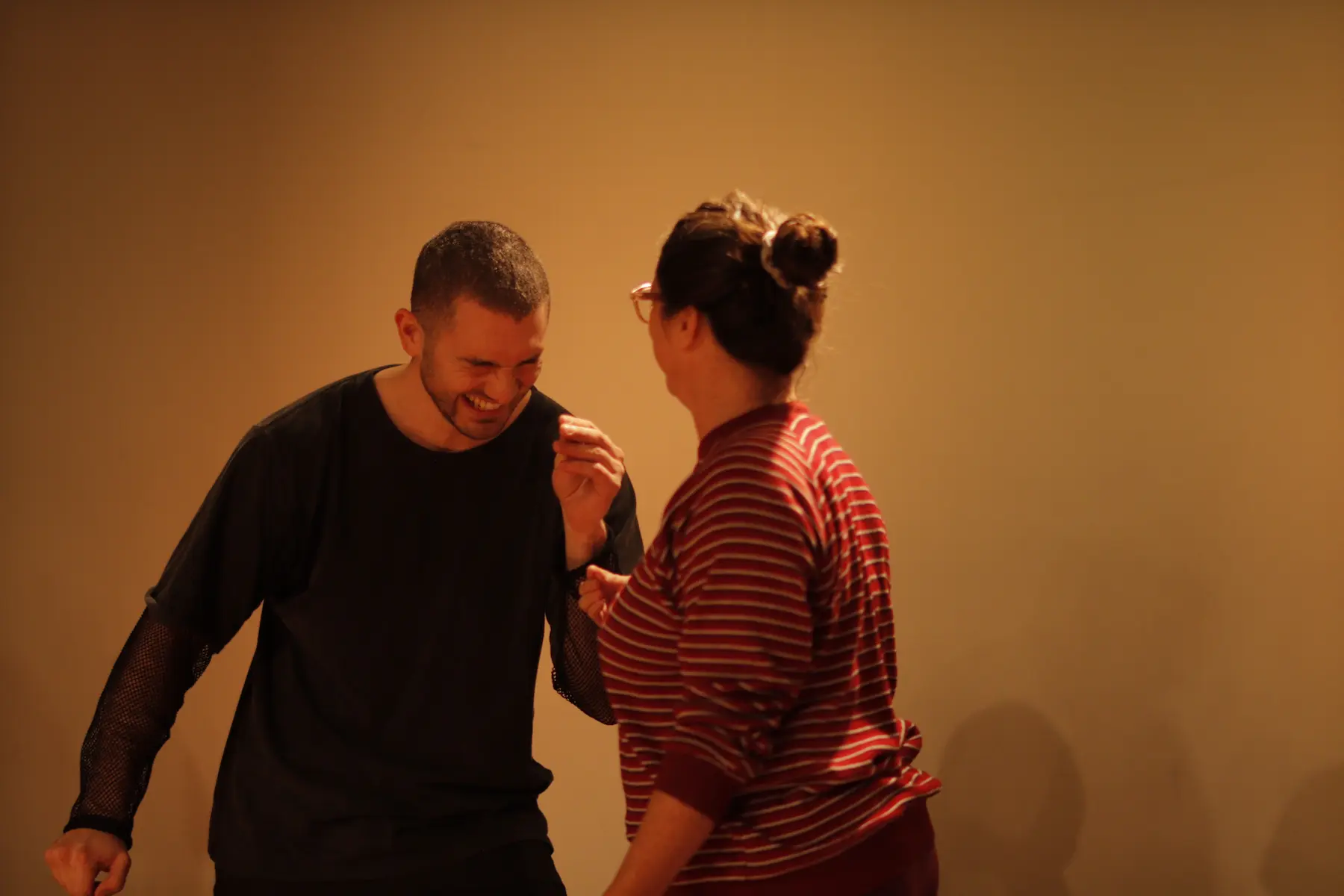 un hombre riendo y una mujer de espaldas en un escenario realizando una escena teatral improvisada
