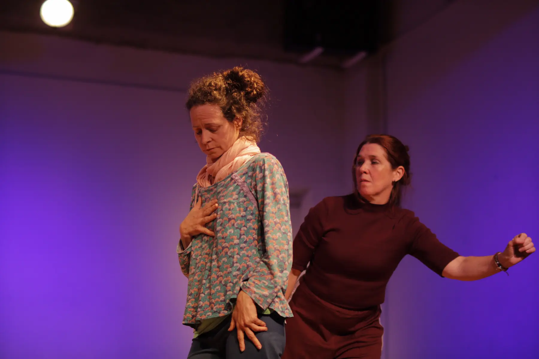 Dos actrices en una escena de improvisaci贸n teatral, una con expresi贸n seria mirando hacia abajo y la otra detr谩s en una postura activa.