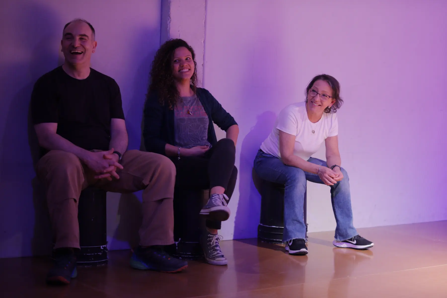 Un actor y dos actrices sentados sobre tachos plásticos se ríen ante una indicación durante una escena de improvisación teatral