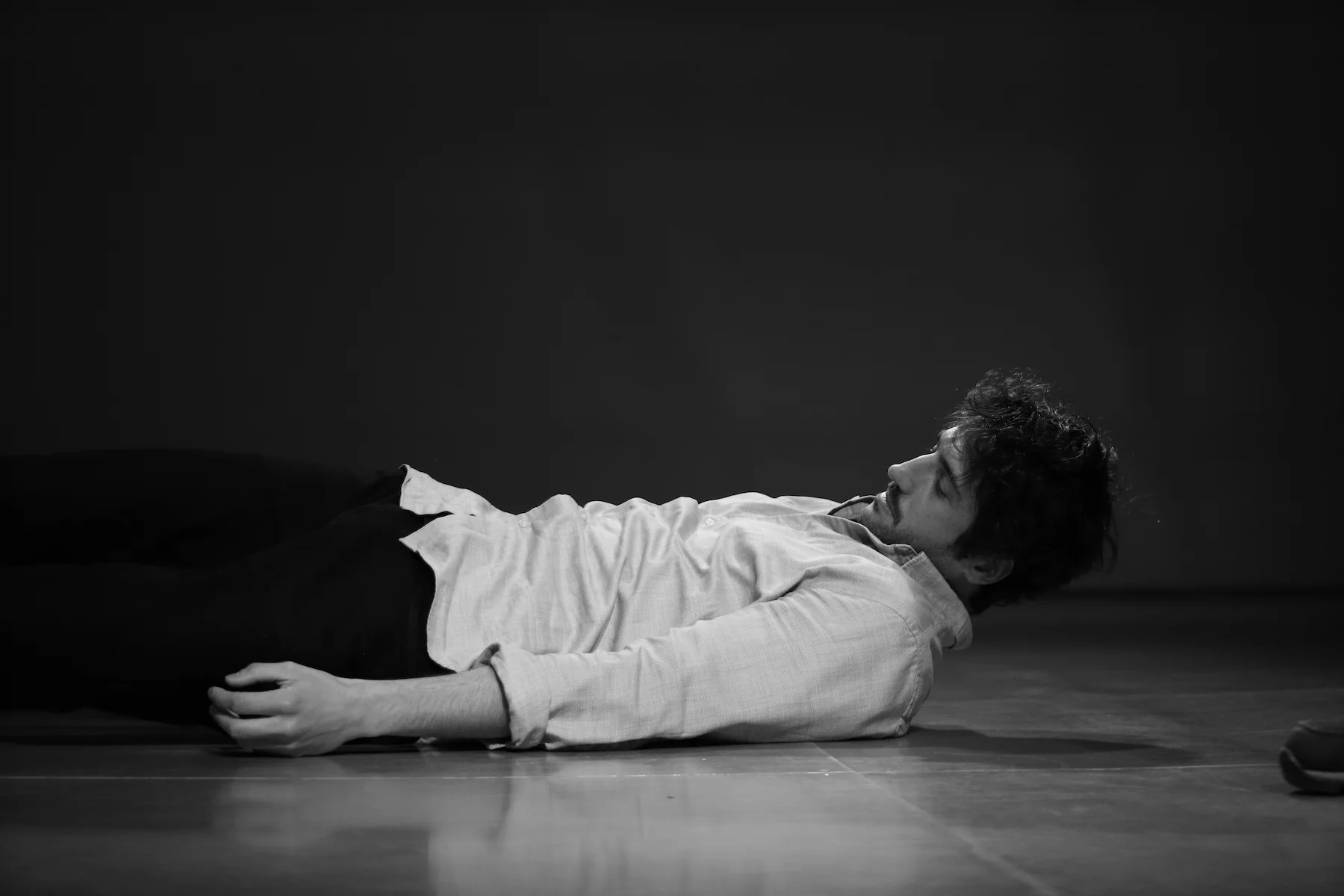 Un actor en el suelo, esforzándose por levantarse, con una expresión concentrada mientras improvisa una escena teatral