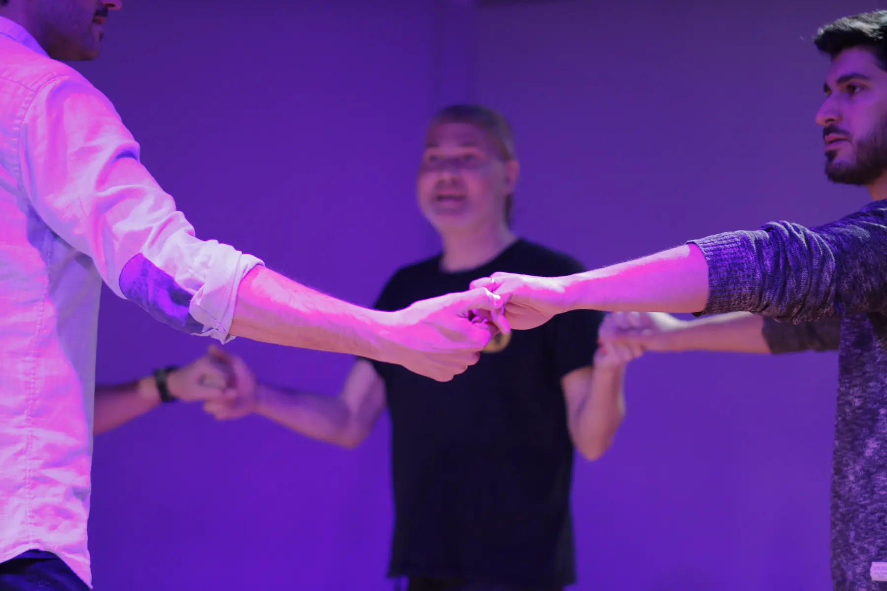 Tres hombres tomados de las manos forman un círculo, interpretando una escena de improvisación teatral